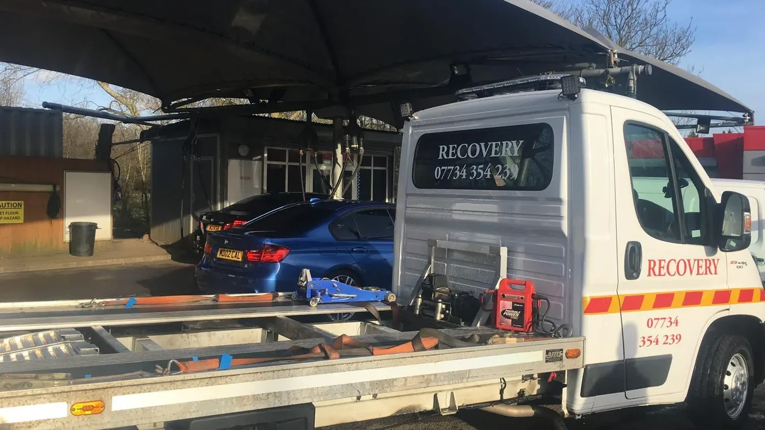 White tilt bed recovery truck signwritten Recovery 07734 354239, with straps, a trolley jack and a booster pack on the empty bed